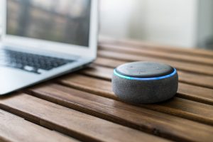 Assistente virtual Alexa sobre uma mesa, ao lado de um notebook.