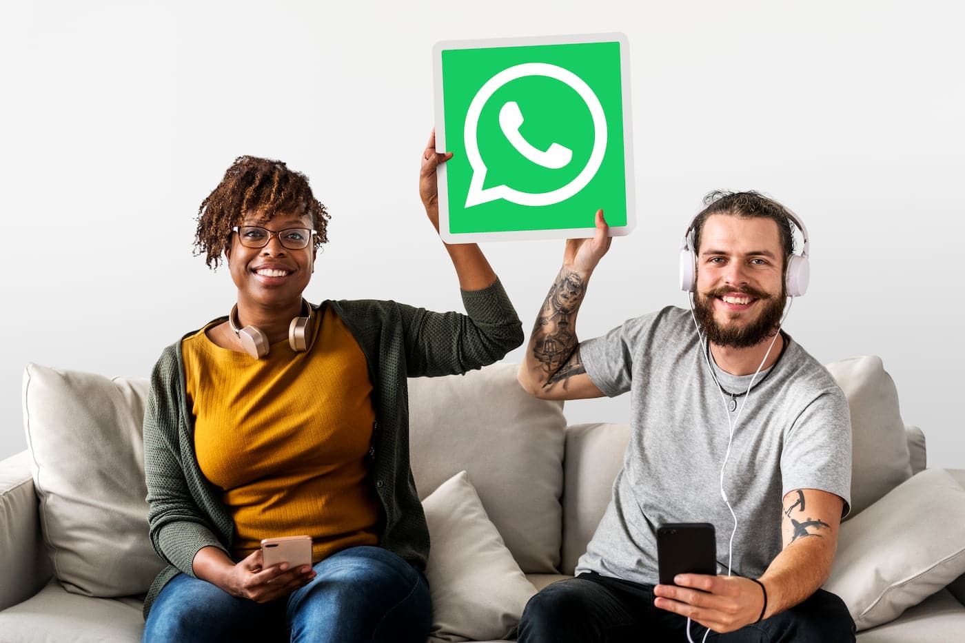 Mulher e homem sentados em um sofá segurando uma placa com ícone do WhatsApp.